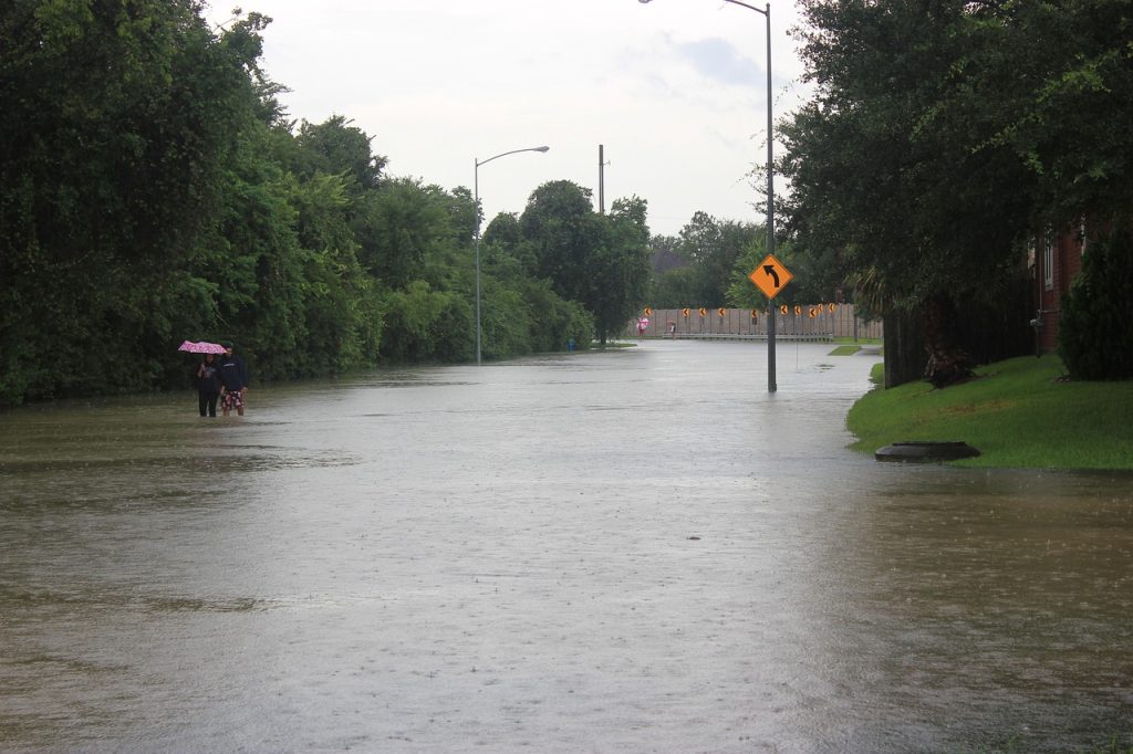 Hurricane Harvey 2017 - flooded street shown with people walking with an umbrella and road signs showing the depth of the water where a road used to be.