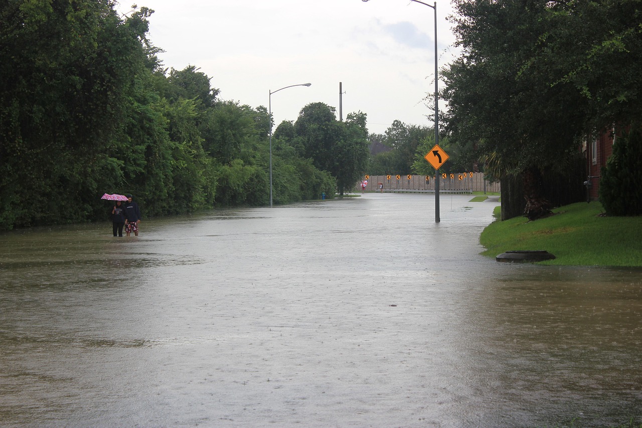 Hurricane Harvey 2017 - flooded street shown with people walking with an umbrella and road signs showing the depth of the water where a road used to be.