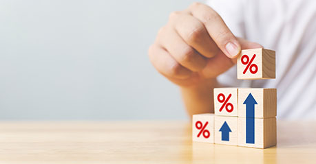 A person stacking wooden blocks on a table, the blocks have % symbols with each stack getting higher showing an increase