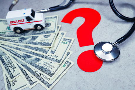 Toy Ambulance sitting on several hundred dollar bills with a stethoscope and question mark next to it