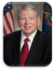 A photo of Mr. Ford wearing a suit in front of American and Pennsylvanian flags.