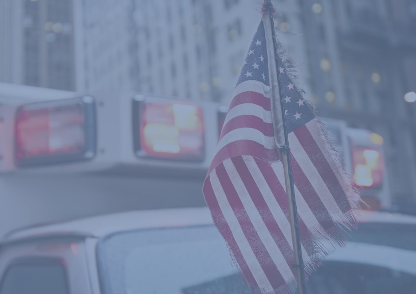 An American flag waving in front of an ambulance with the emergency lights on.